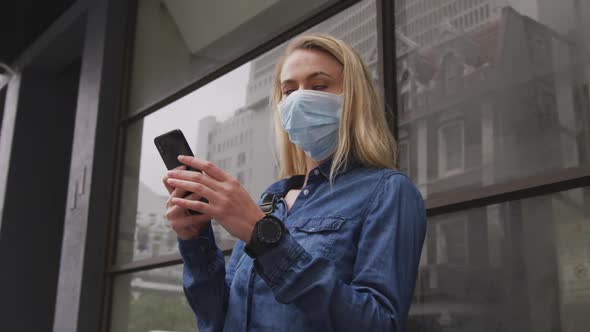 Low angle view of Caucasian woman wearing a coronavirus Covid19 mask and using her phone