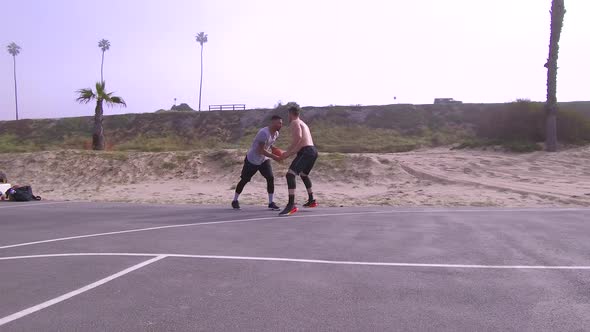 A man does a slam dunk while playing one-on-one basketball hoops on a beach court.