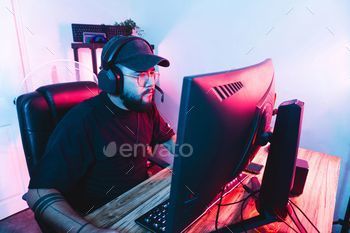Hispanic professional gamer wearing headphones immersed in playing an online game on his computer