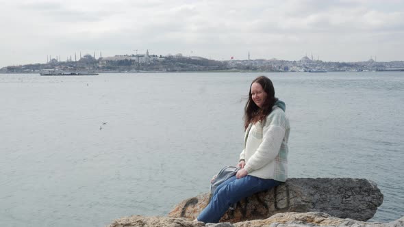 Smiling Mature Woman Sitting on Rock at Watereway