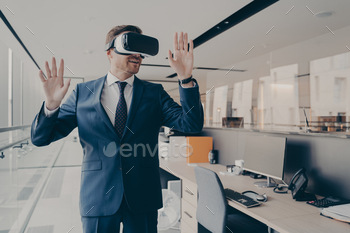 Businessman in VR glasses enjoying virtual tour, exploring digital reality, standing in office