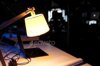 Laptop in a dark room illuminated by a table lamp