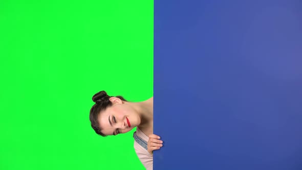 Girl Looking Out From Behind Blue Blank Placard on Green Screen at Studio