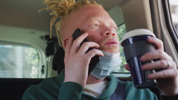 Albino african american man wearing face mask sitting in car talking on smartphone