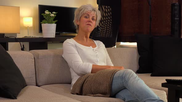 A Friendly Middle-aged Woman Sits on a Couch in an Apartment Living Room and Talks To the Camera