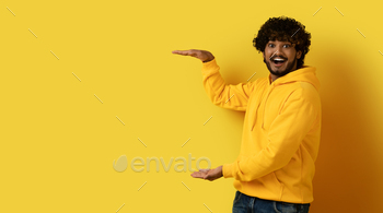 aring casual outfit holding something invisible transparent in his hands and smiling at camera, isolated on yellow background