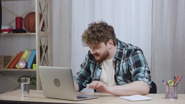 Young Man in Checkered Shirt Typing on Laptop Keyboard and Enjoying Good News or Deal