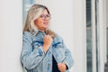 Beautiful blonde woman in glasses and a denim jacket. Urban portrait. Side view. - PhotoDune Item for Sale