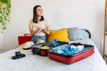 Young beautiful woman sitting on bed packing her suitcase for travel vacation
