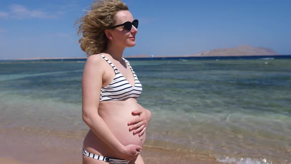 Happy Pregnancy On Vacation Concept. Pregnant Woman Walking On Beach.