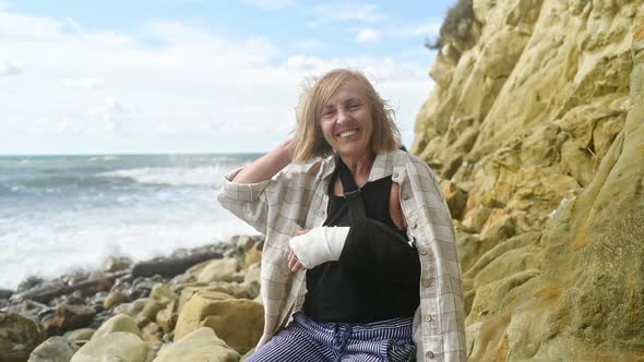 Senior Elderly Woman Relaxing Sitting on Coast of Ocean or Sea Windy Cloudy Day Suffering From Pain