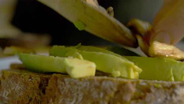 Closeup of female putting mushrooms on avocado toast. Young woman makin healthy lucnh at home. Slow