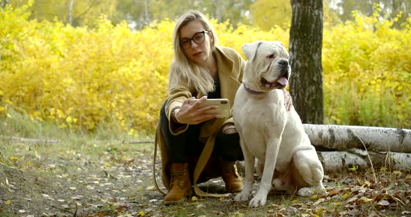 Close - Up of a Blond Young Girl in a Coat and Boots. She Is in the Woods, Squatting Next To His Big