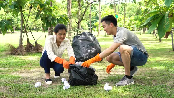 Young Asian Man and Woman Collecting Trash in Garbage Bag in the Park