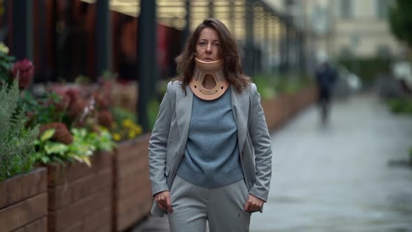 a Middleaged Woman with an Orthopedic Collar Around Her Neck and a Gray Suit is Scowling Down the