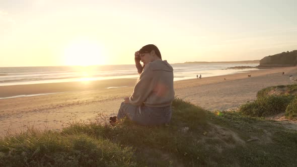 Traveling woman sitting on hill against sunset sky near sea