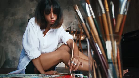 Lady Artist is Drawing a Picture on Canvas Using Oil Paints While Sitting on a Floor at Her Art