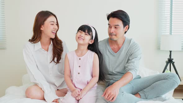 Portrait of Asian happy family wear pajamas smile and look at camera on bed in vacation at home.