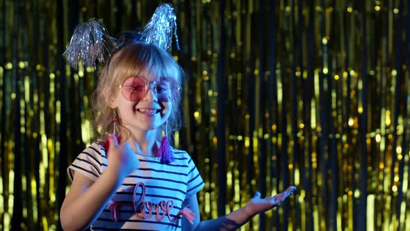 Trendy Girl in Stylish Glasses Standing on Blue Neon Lights Pointing at Blank Space Agree Sign