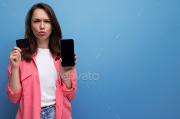 brunette young woman in pink shirt and jeans with phone and money card mockup on studio isolated