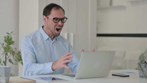 Middle Aged Man Feeling Shocked While Using Laptop in Office