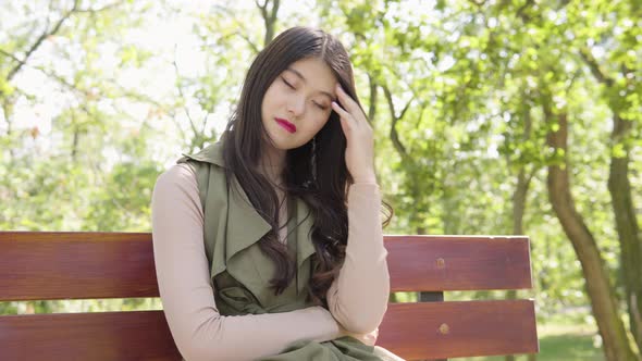 Young Asian Woman Thinks About Something As She Sits Bench Park Sunny Day