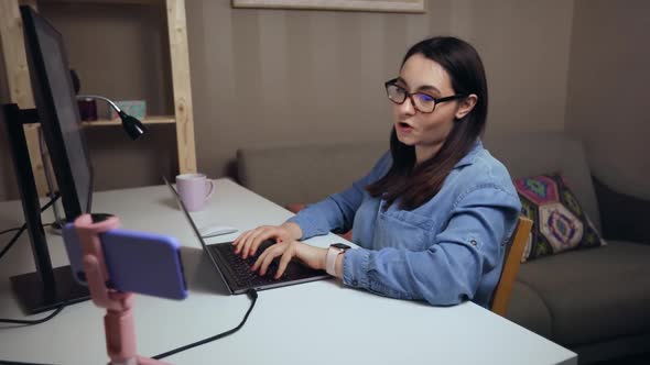 Young Woman Talking to Mobile Phone Recording Video While Using Laptop at Home