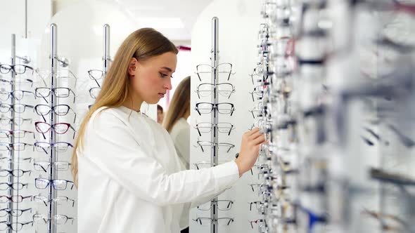 Lovely girl choosing glasses in the store. Attractive young woman buying fashionable eyeglasses. Vis