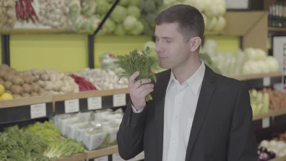 Portrait of Smiling Caucasian Man Smelling Fresh Bunch of Greenery in Grocery Store. Young Guy in