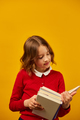 Portrait of happy schoolgirl reading a book on yellow studio - PhotoDune Item for Sale