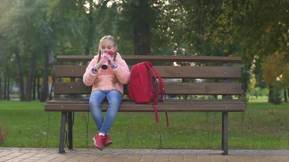 Happy Schoolgirl With Rucksack Drinking Tea From Thermos Cup as Sitting on Bench