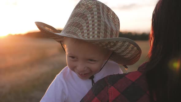 Happy Little Toddler Boy in Hat Having Fun Sitting in Parents Arms in Field in Summer at Sunset