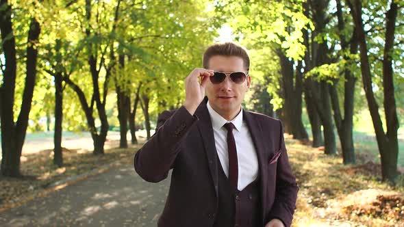 Close-up of a Successful Businessman Putting on Sunglasses in Autumn Park.