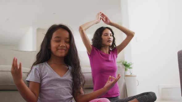 Hispanic mother and daughter sitting on the floor meditating at home