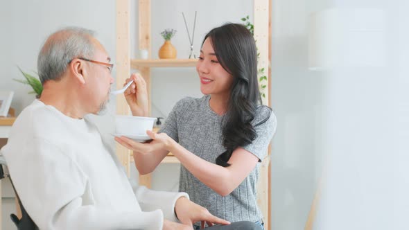 Asian senior elderly father eat salad with daughter in kitchen at home.