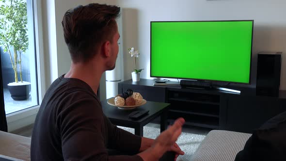 A Man Watches a TV with a Green Screen, Then Turns To the Camera and Talks To You with a Smile