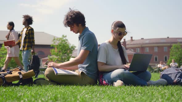 Couple of Students Sitting in Park and Studying with Laptop and Textbook