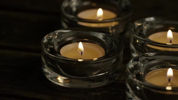 Tea candles with flaming wicks on a wooden background - CANDLES 020