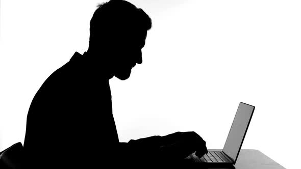 Silhouette of Cheerful Man Celebrating Success While Working on Laptop