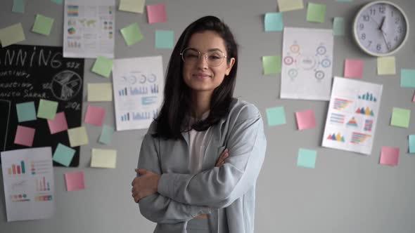 Happy young hipster teen girl wearing glasses looking at camera and posing indoors in modern office