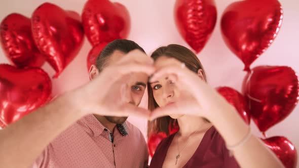 Happy Beautiful Young Woman and Handsome Man Making Heart Shape Hand Gesture