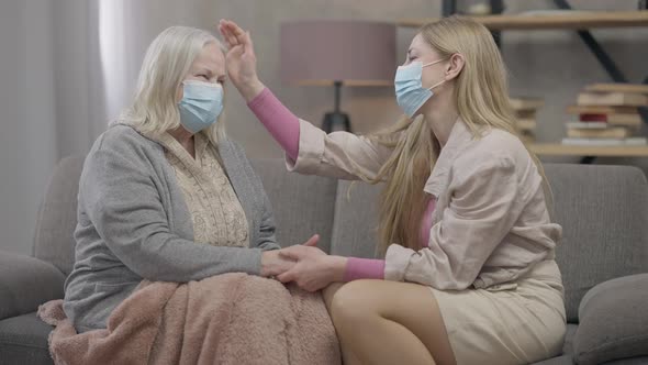 Side View Portrait of Two Positive Senior Women in Coronavirus Face Masks Talking Holding Hands