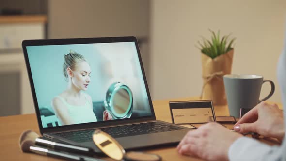 Young Woman Learn How to Apply Makeup While Watching a Female Beauty Blogger's Lesson on a Laptop