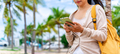 Young woman traveler relaxing and using a mobile phone by a tropical beach while traveling - PhotoDune Item for Sale