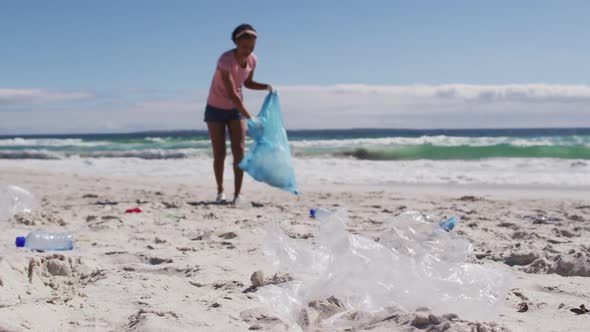 African american woman collecting plastic waste on the beach