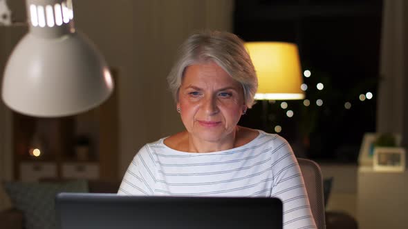 Happy Senior Woman with Laptop at Home in Evening