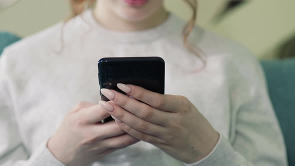 Beautiful Caucasian Woman In Beige Sweater Sitting On A Sofa And Using Smartphone