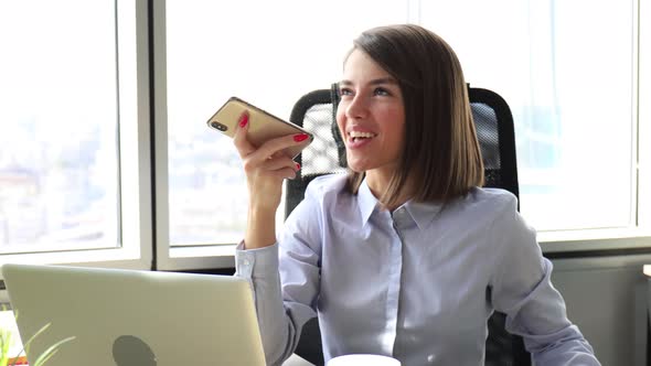 Confident businesswoman holding smartphone near mouth for recording voice message