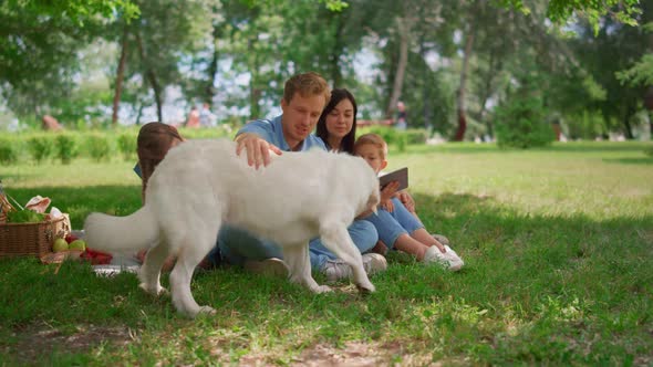 White Dog Lie Down Near Family Holding Tablet on Picnic