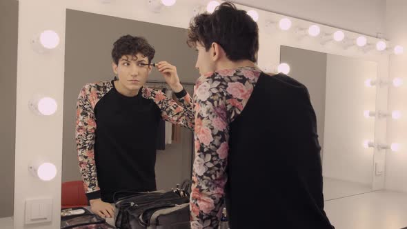 Androgynous Man Paints Eyelashes in Front of a Mirror